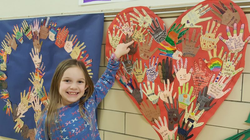 A first grade student is proud to show her art work